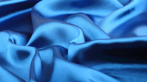 Close-up of luxurious blue satin fabric showing soft folds and a lustrous, light-reflecting surface.